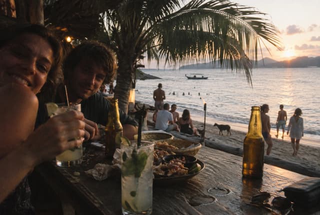 Friends sharing drinks at a beach table near sunset